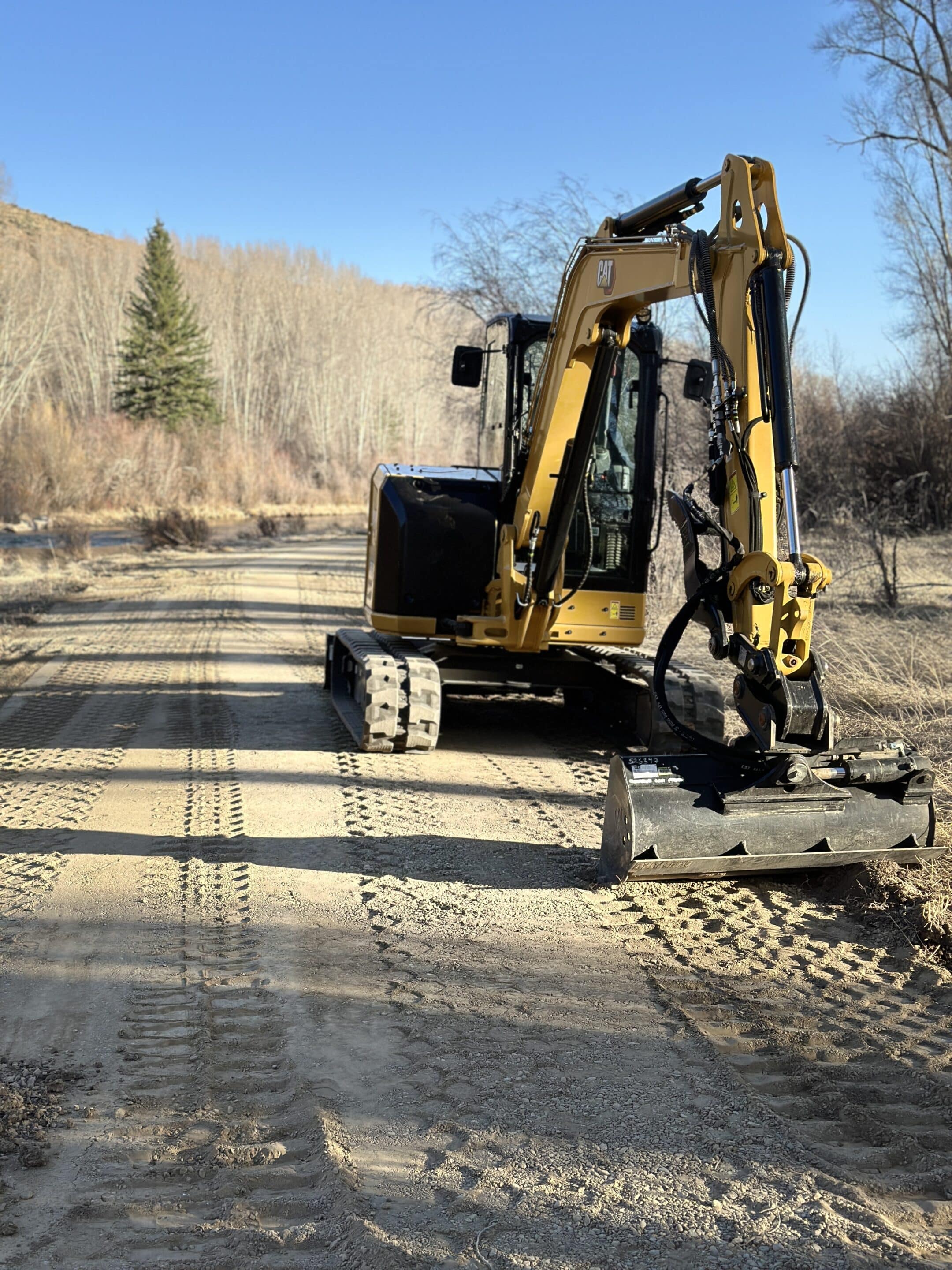 CAT excavator parked on a dirt road near a line of trees.