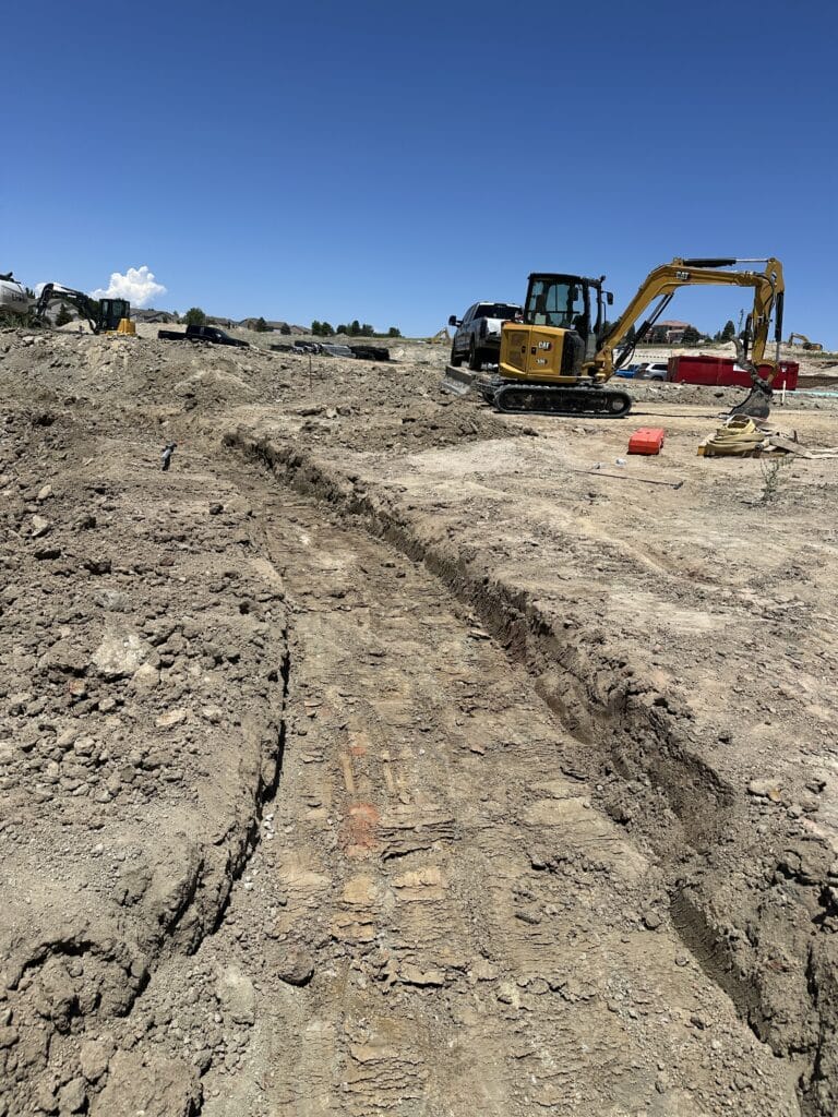 Yellow mini excavator near a long dirt trench.