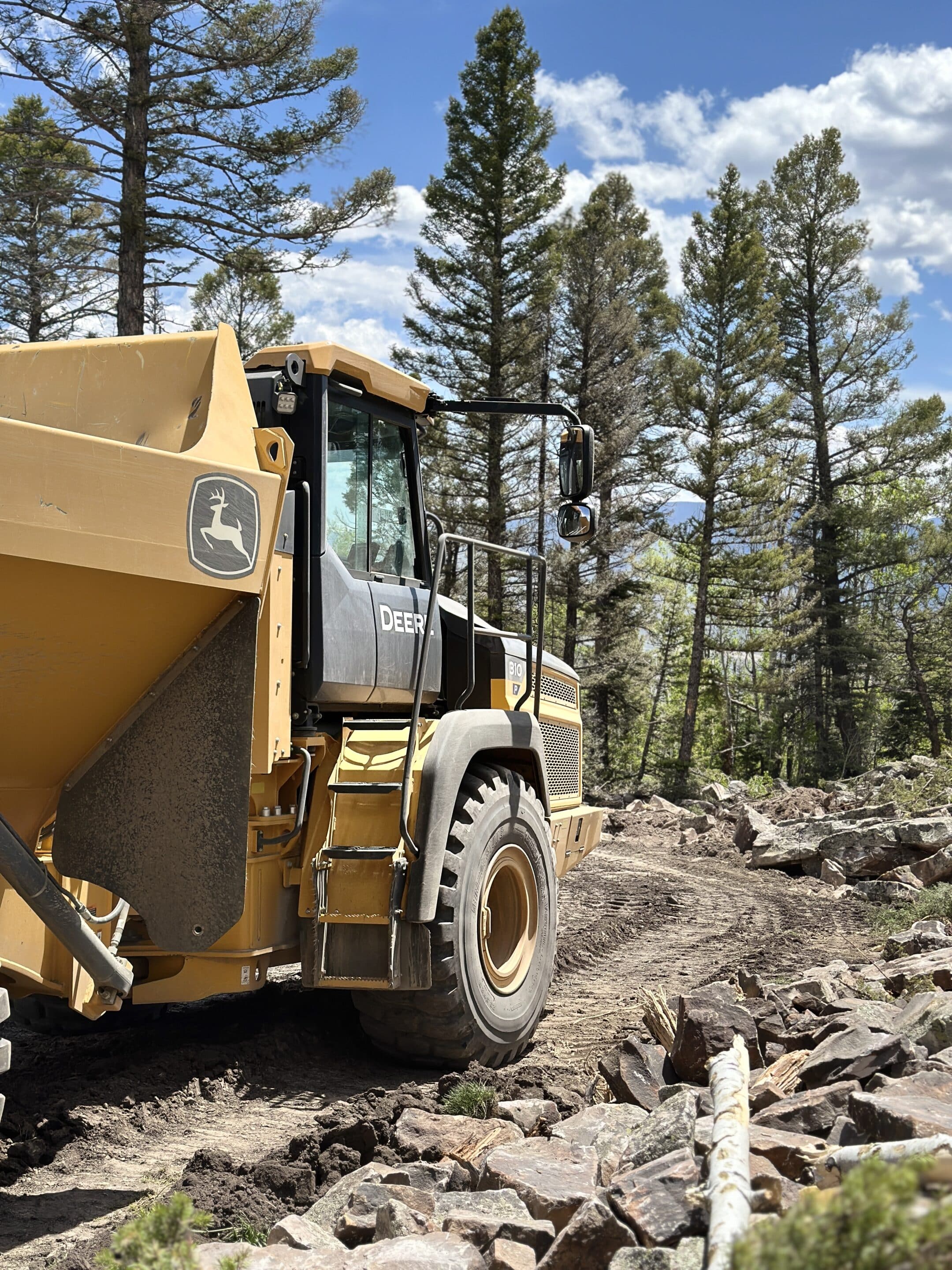 John Deere dump truck on a rocky path in a pine forest.