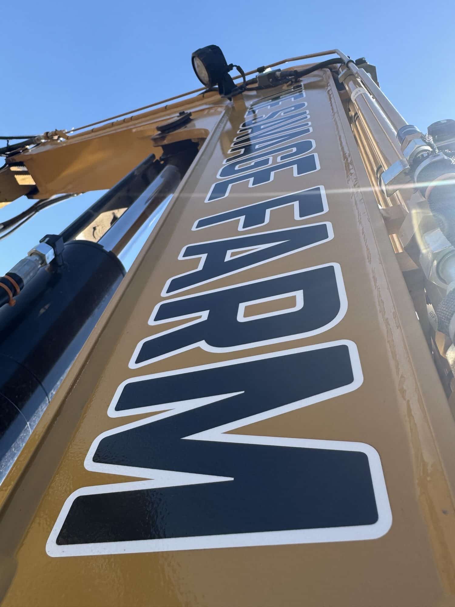 CAT excavator parked on a dirt road near a line of trees.